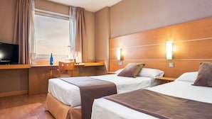 Una habitación de hotel con dos camas, un escritorio, un televisor y una ventana con cortinas.