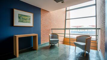 Una habitación moderna con pared azul, un cuadro enmarcado, una consola de madera, dos sillas y un ventanal con vistas.