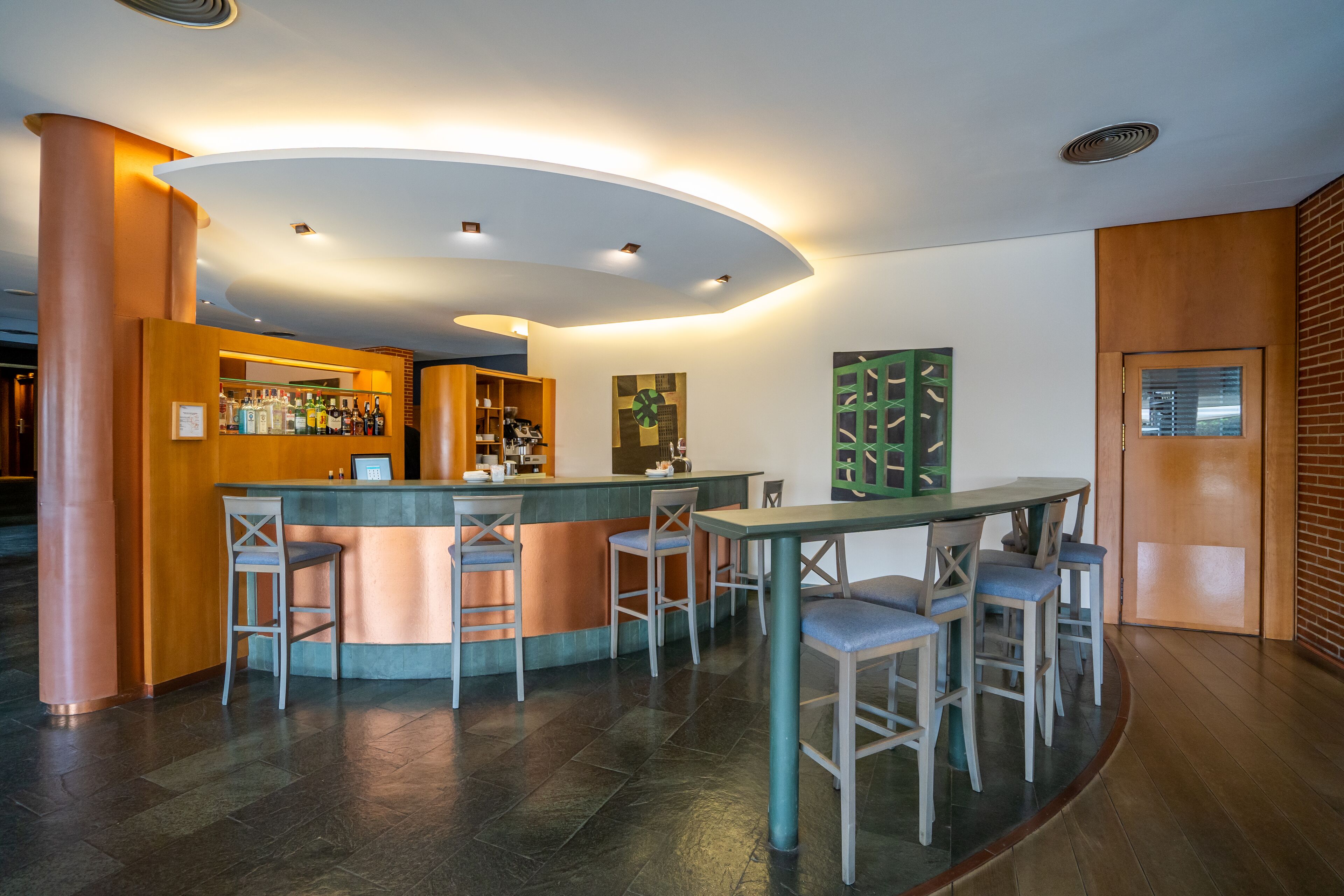 A bar area with a curved counter, multiple stools, and a table with chairs.