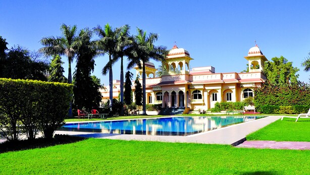 Um edifício grande com piscina, cercado por palmeiras e gramados bem cuidados.