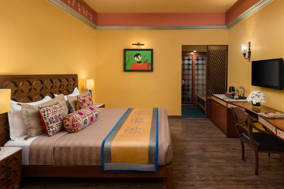 Una habitación de hotel con cama, mesita de noche, lámpara, escritorio, silla y televisor.