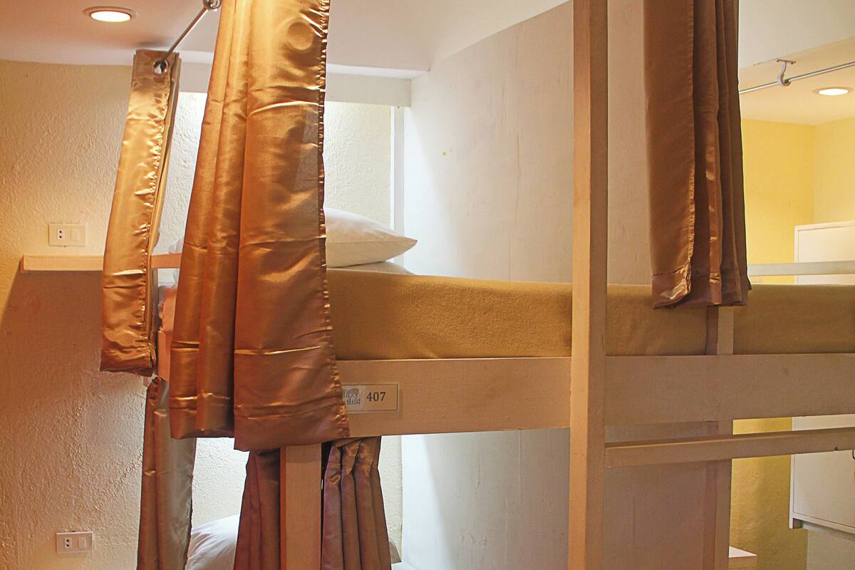 Habitación con literas, cortinas, una cama a la vista y un estante pequeño.
