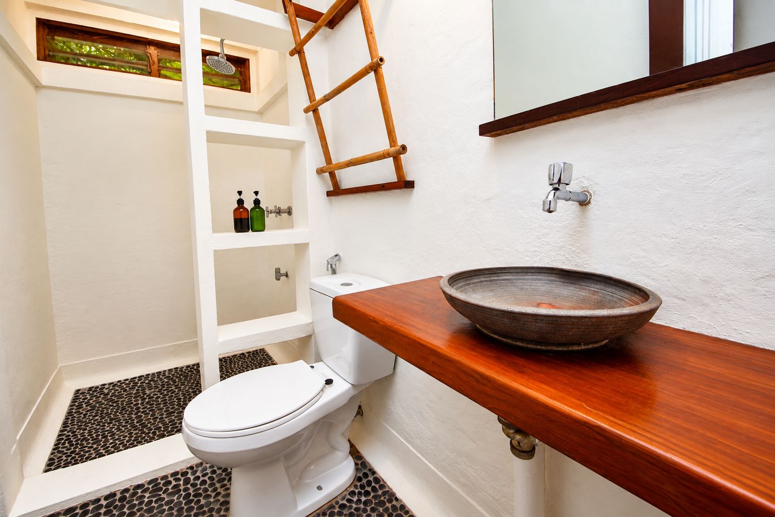 A bathroom with a white toilet, a wooden vanity with a bowl sink, a shower with a glass door, and a ladder against the wall.