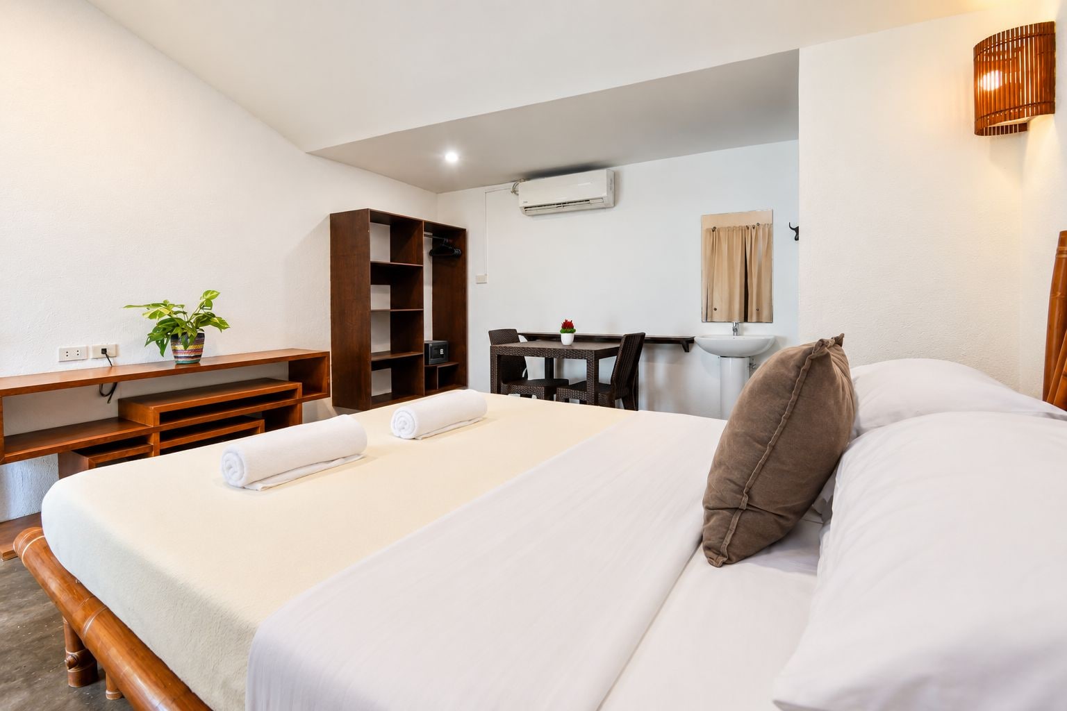 A hotel room with a bed, a desk, a chair, a wardrobe, and a small table with a plant.