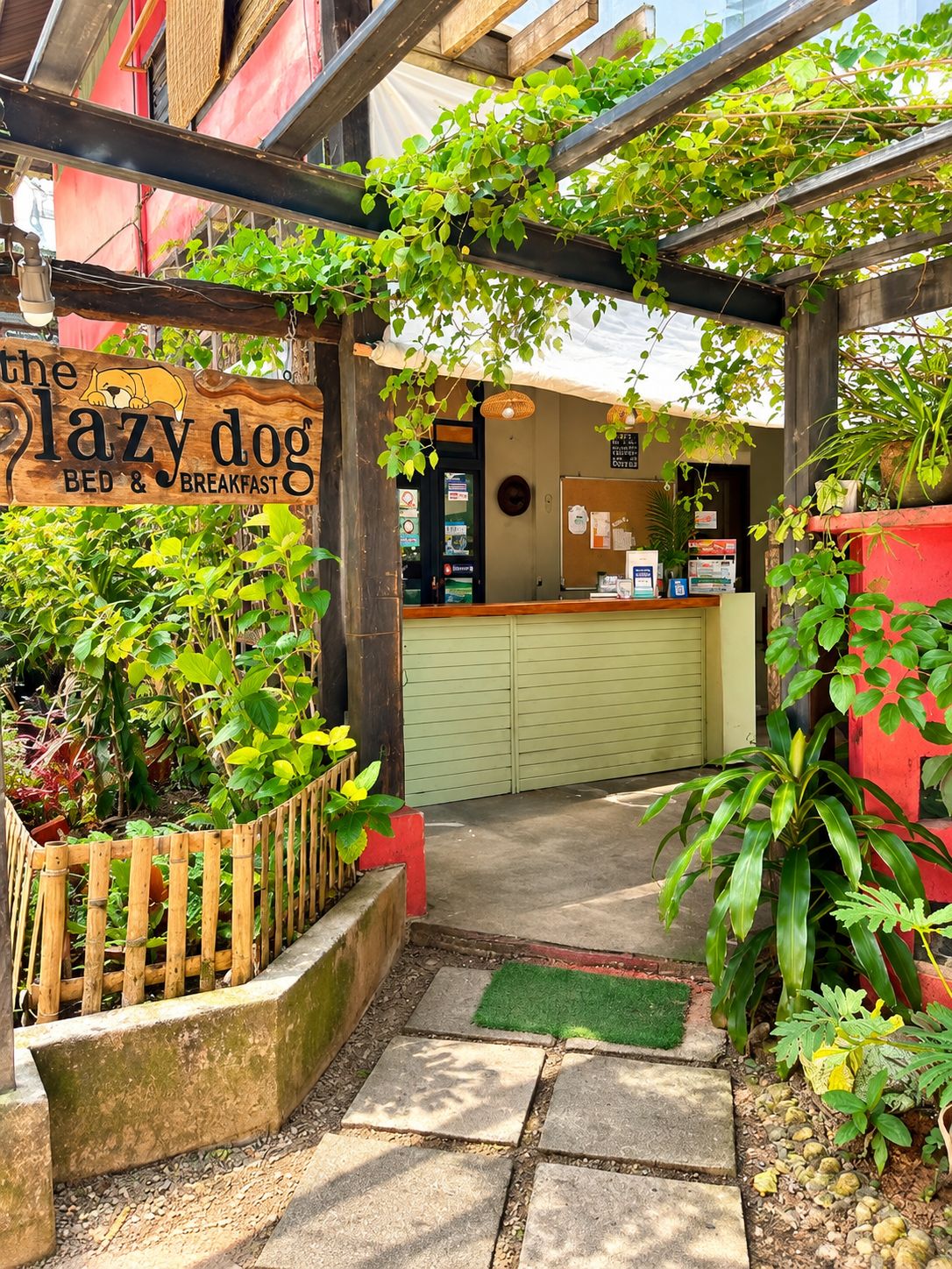 A cozy outdoor seating area with a wooden pergola, a sign for 'The Lazy Dog Bed & Breakfast,' and a counter with a menu board.