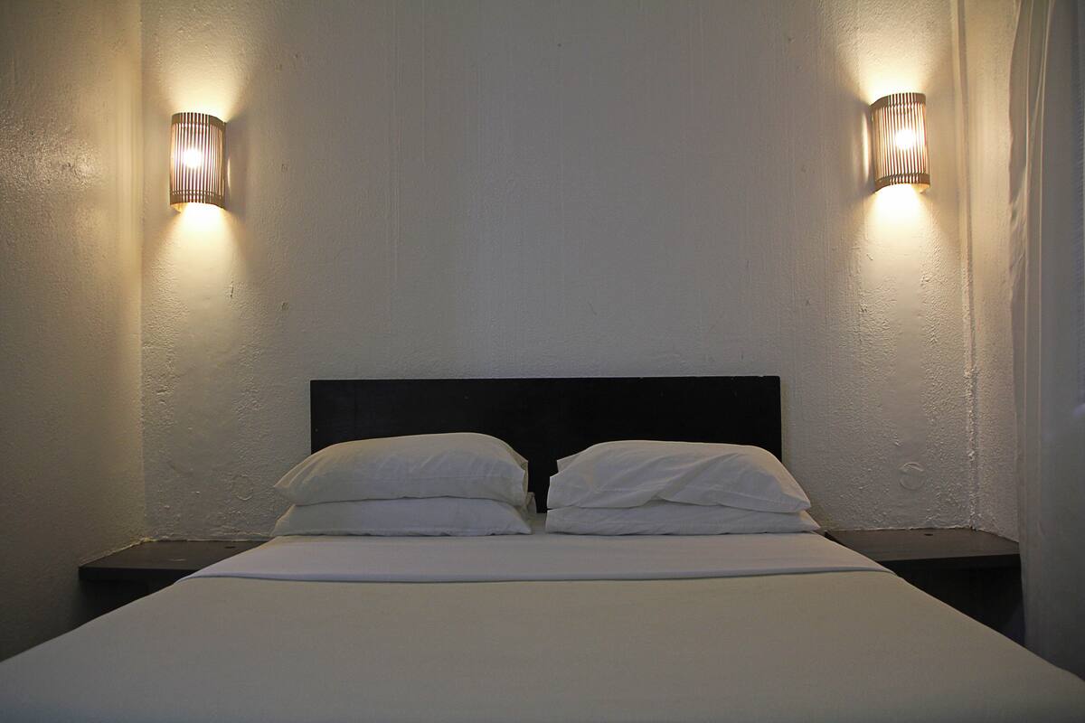 Una cama con sábanas blancas y dos lámparas de pared a cada lado.