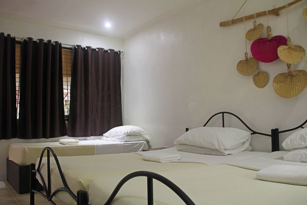 Habitación de hotel con dos camas individuales, una ventana con cortinas oscuras y un cesto decorativo colgado en la pared.