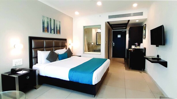 A modern hotel room with a large bed, bedside tables, a flat-screen TV, and a bathroom visible through an open door. - The HQ (Vasco da Gama)