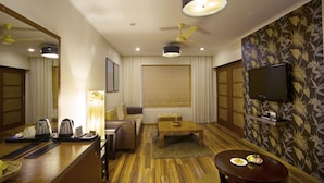 A hotel room with a wooden floor, a sofa, a coffee table, a TV mounted on the wall, and a window with curtains. - The HQ (Vasco da Gama)