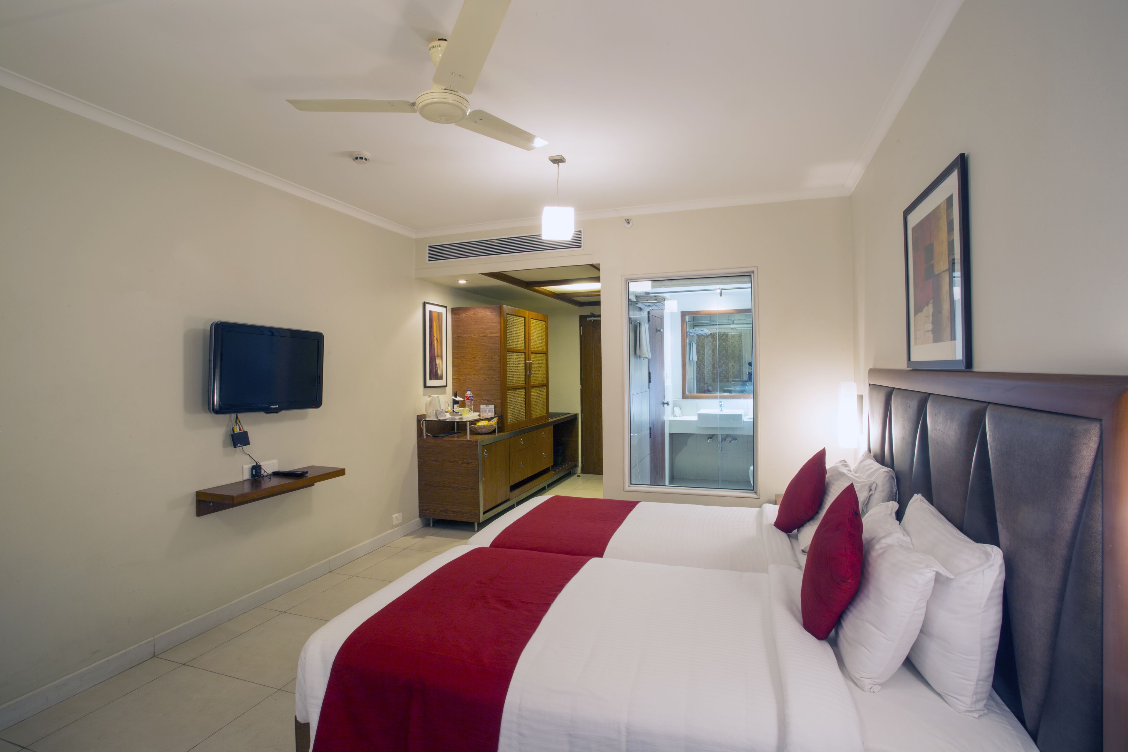 Une chambre d’hôtel avec un lit, un téléviseur posé sur une étagère, un ventilateur de plafond et une vue sur la salle de bain.