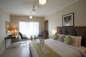 A hotel room with a bed, a desk, a chair, a ceiling fan, and a window with curtains. - The HQ (Vasco da Gama)