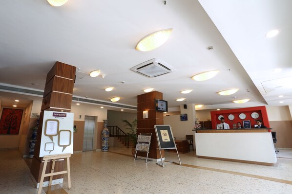 A hotel reception area with a modern design, featuring a reception desk, a digital screen, and a large vase.