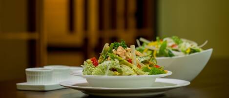 A dining table with two white plates of salad, a white bowl, and a white container.