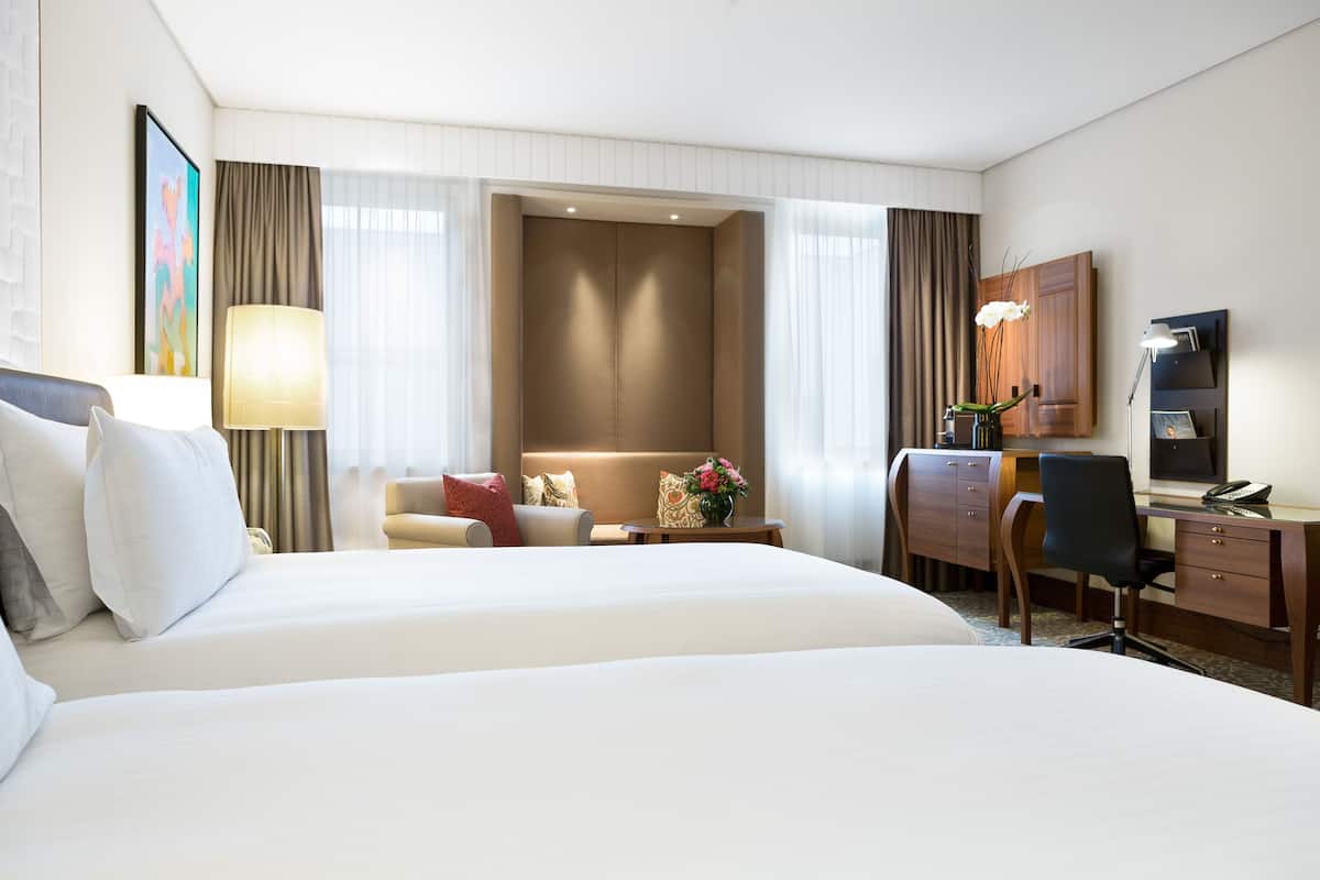A hotel room with a large bed, a desk, a chair, a lamp, and a small table with a vase of flowers.