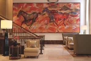 A lobby with a large abstract painting of horses, a staircase, and seating areas.