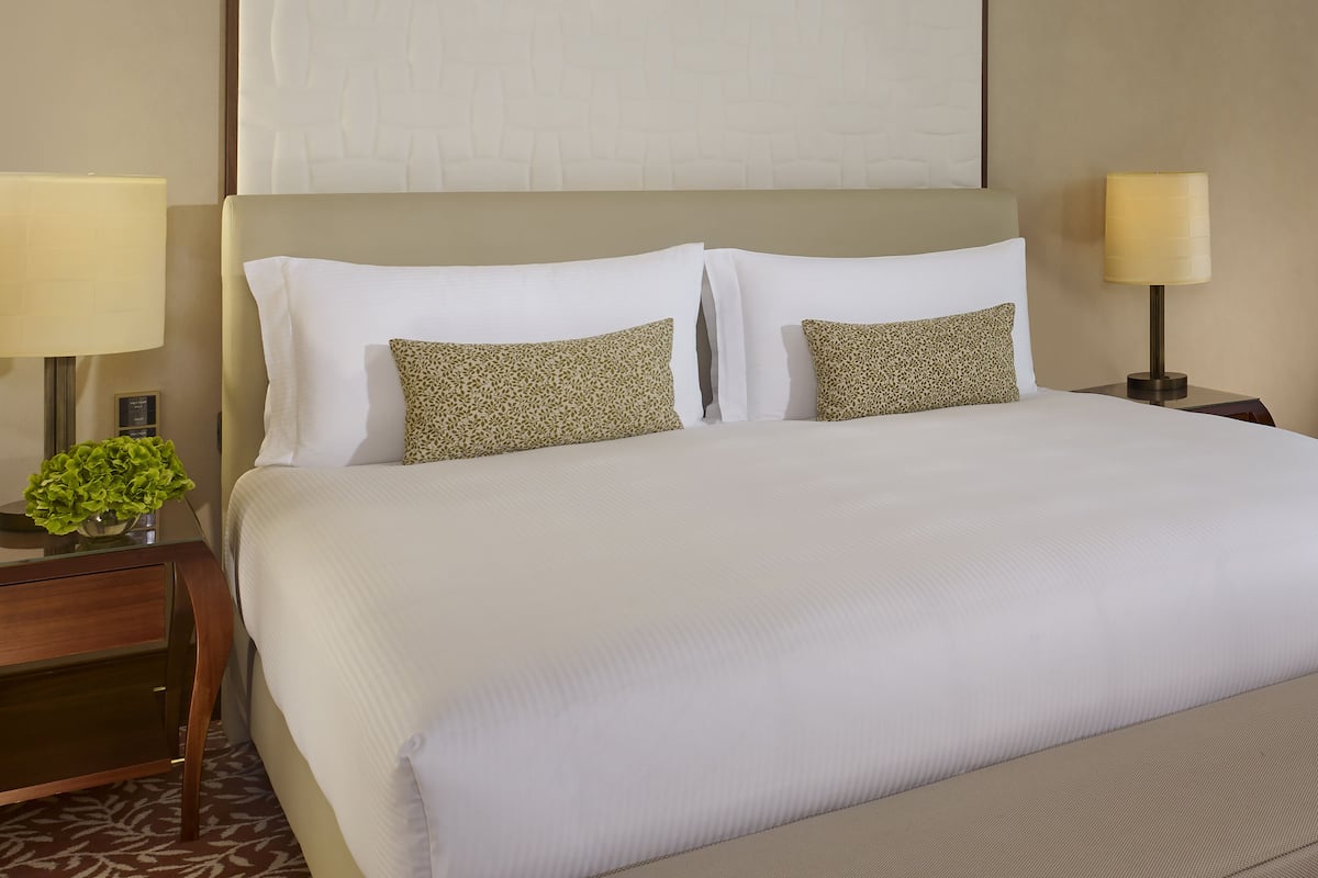 A hotel room with a large bed, two pillows, a nightstand with a lamp, and a small plant.