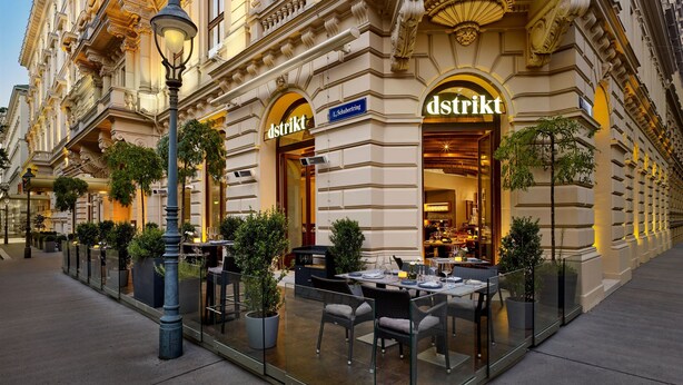 A historic building with ornate architecture, a 'dstrikt' sign, outdoor seating, and a well-lit entrance. - The Ritz-Carlton, Vienna (Vienna)