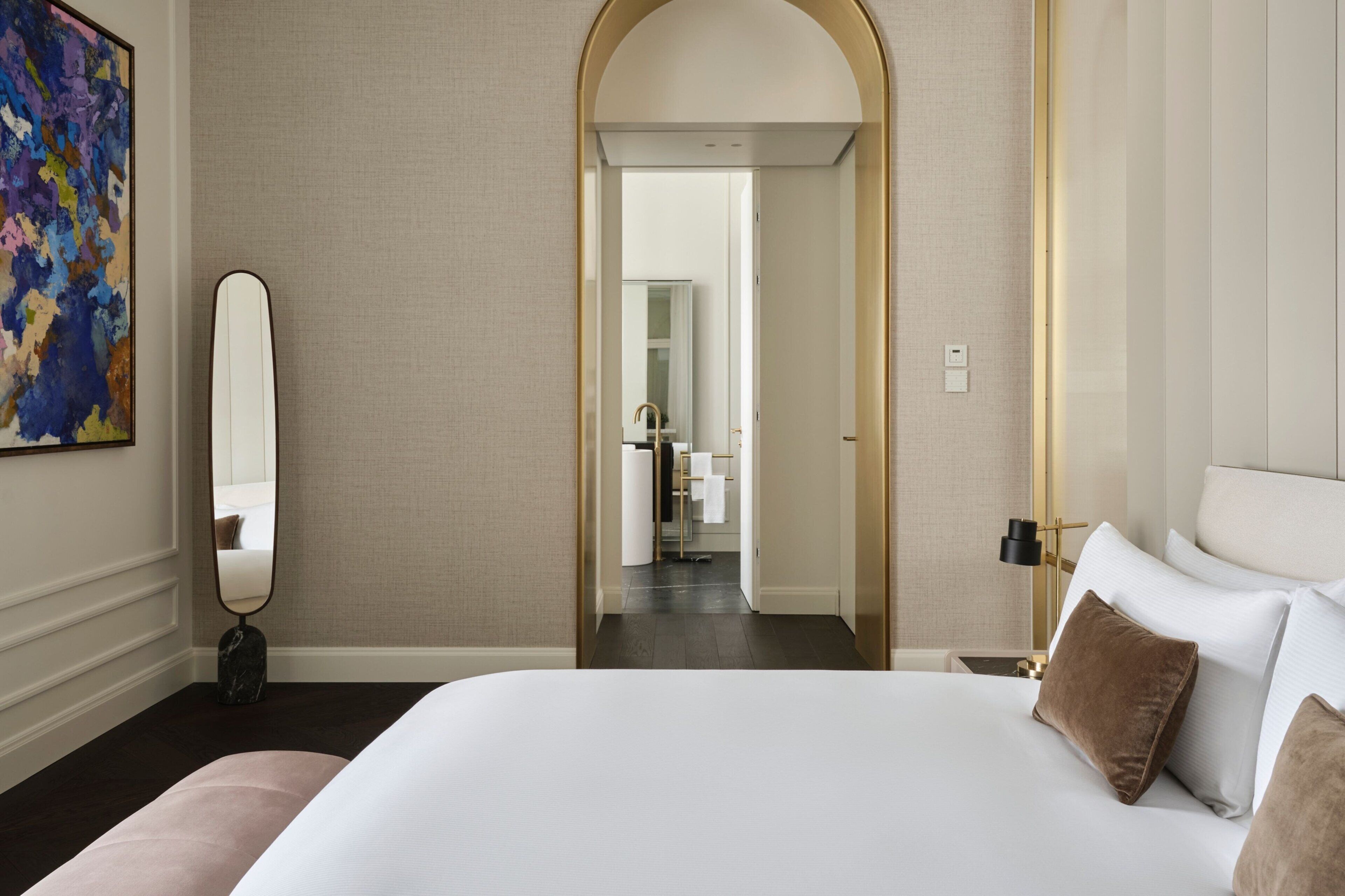 Ein Hotelzimmer mit einem großen Bett, einem Spiegel, einem Gemälde und einer gewölbten Tür zu einem Badezimmer.