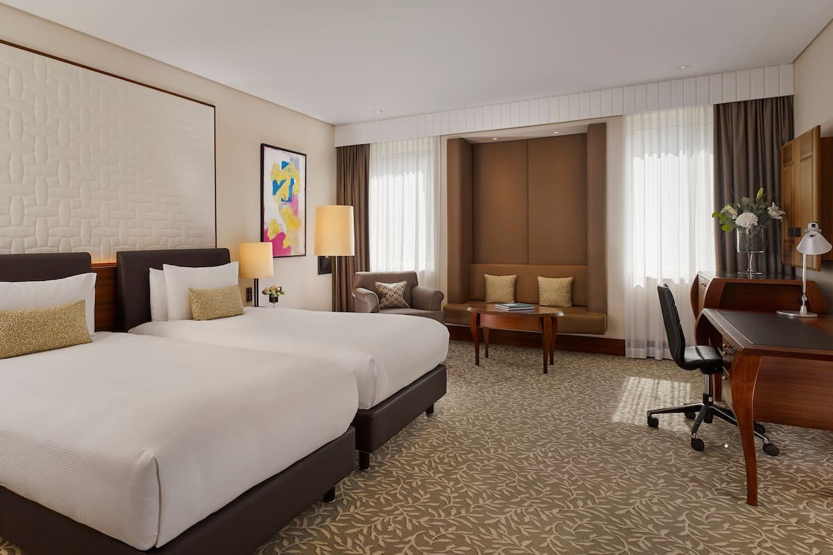 A hotel room with two large beds, a sofa, a desk, and a chair.