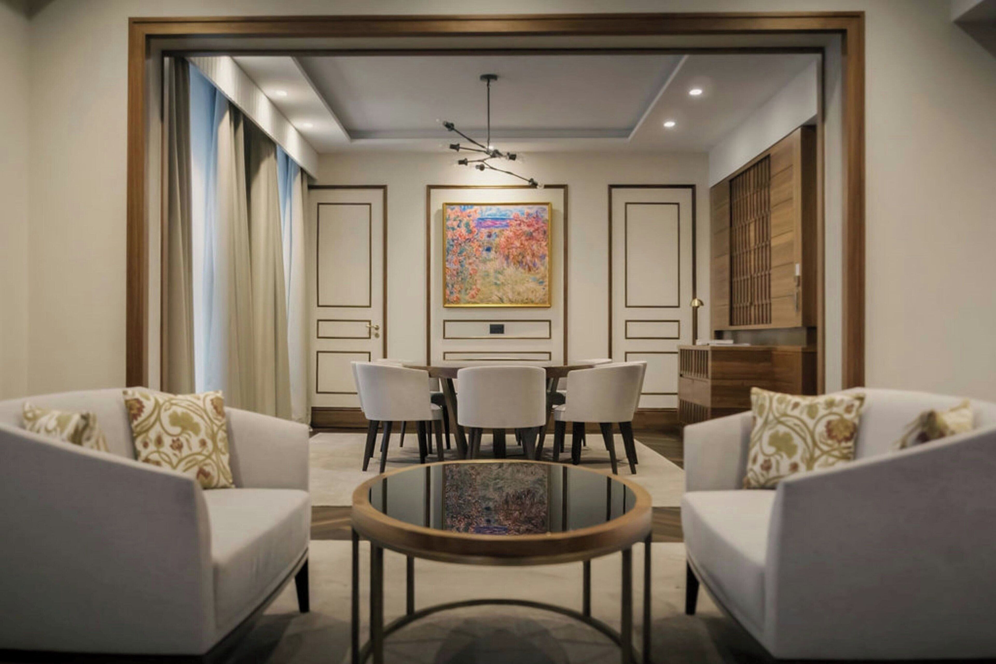 Uma sala de estar moderna com uma mesa de centro redonda, dois sofás, uma mesa de jantar com cadeiras e um quadro abstrato grande na parede.