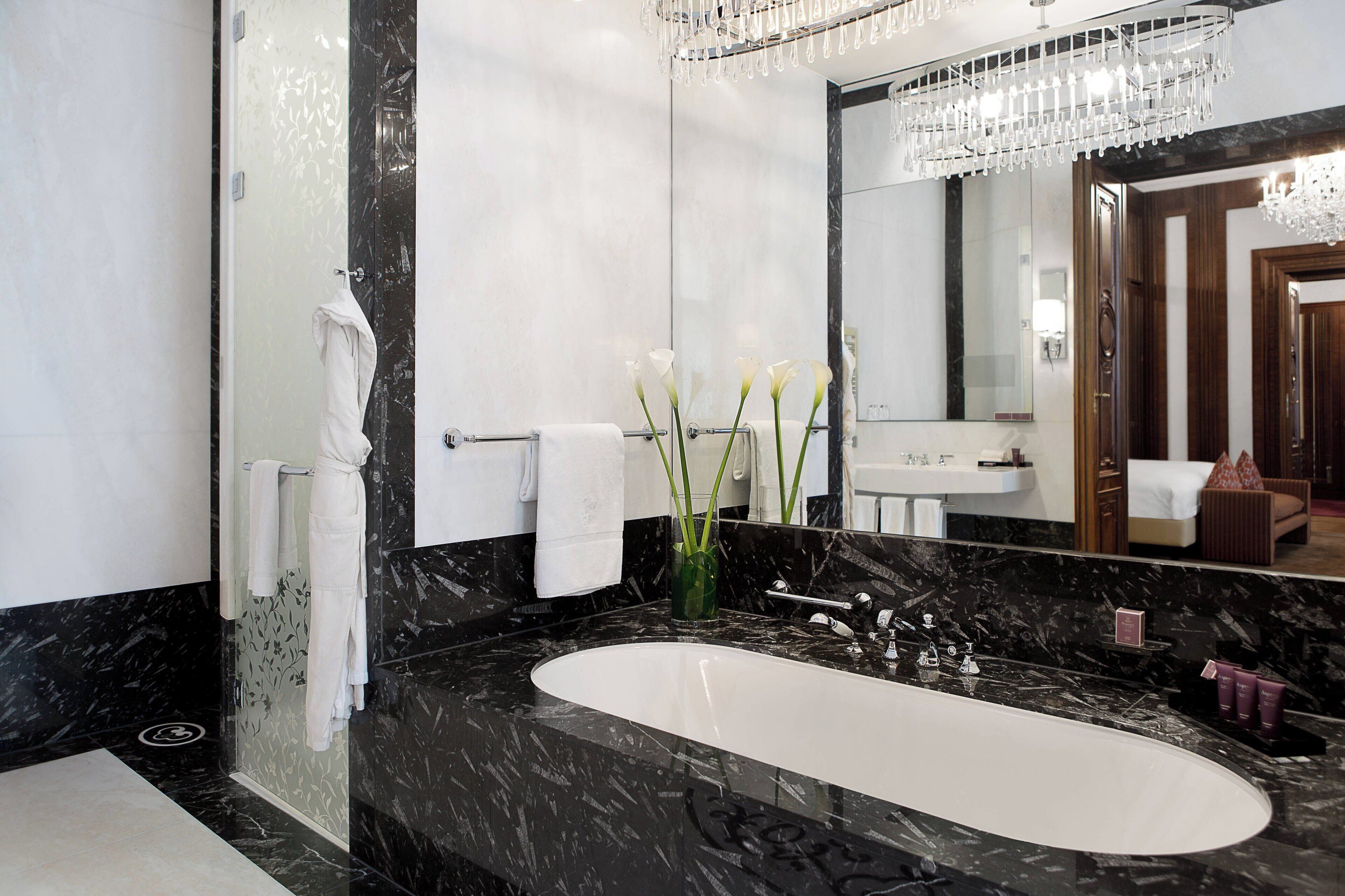 Un baño moderno con lavamanos de mármol negro, un espejo grande y una araña.