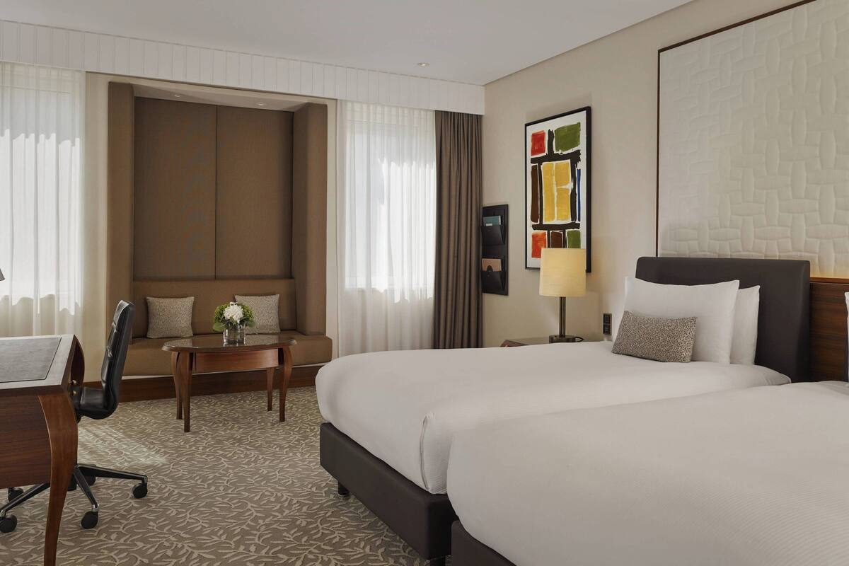 A hotel room with a large bed, a desk with a chair, a sofa, and a small table with a vase.