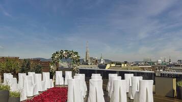 A rooftop venue with white-covered chairs arranged in rows, a floral arch, and a cityscape view in the background.