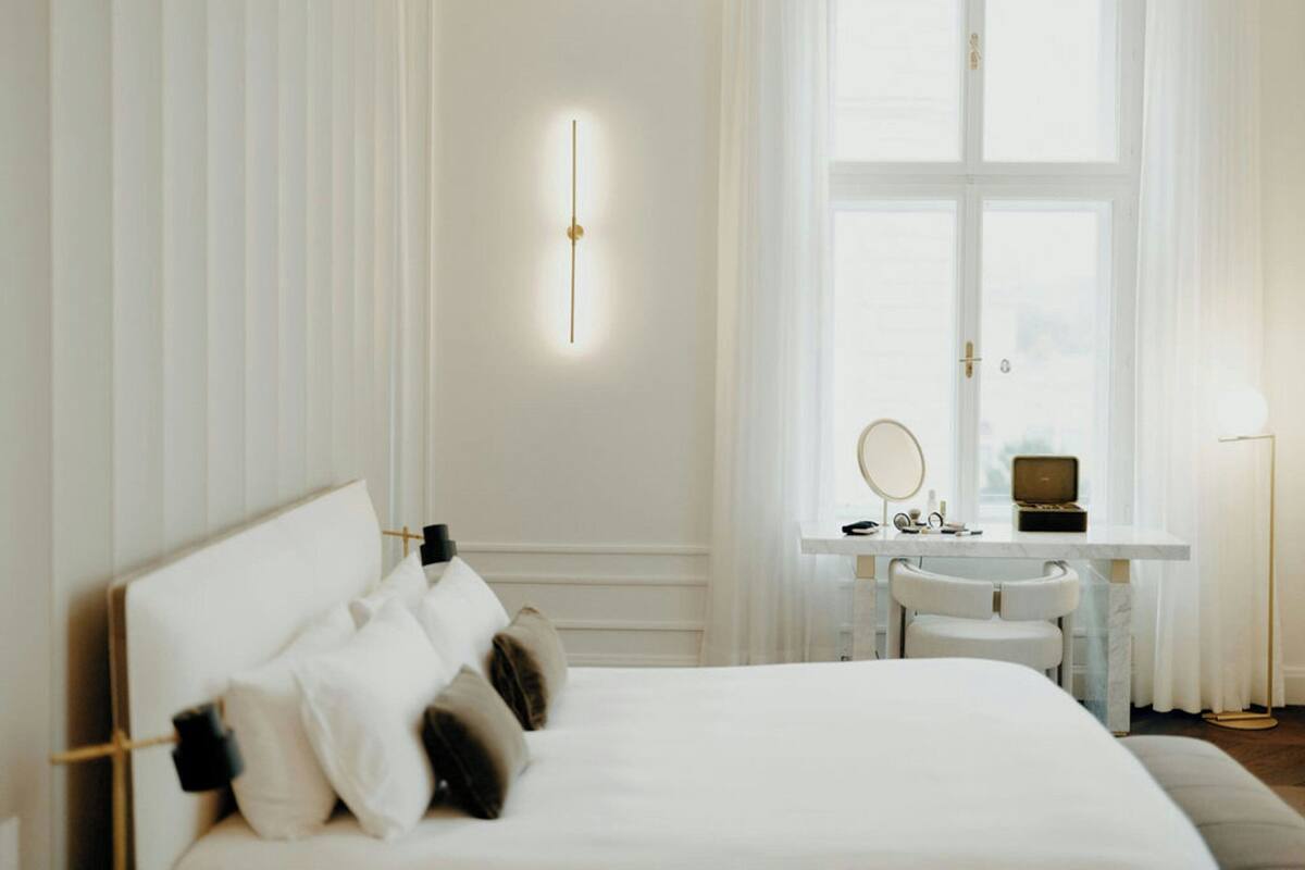 A hotel room with a large bed, a desk with a chair, a mirror, and a window with curtains.