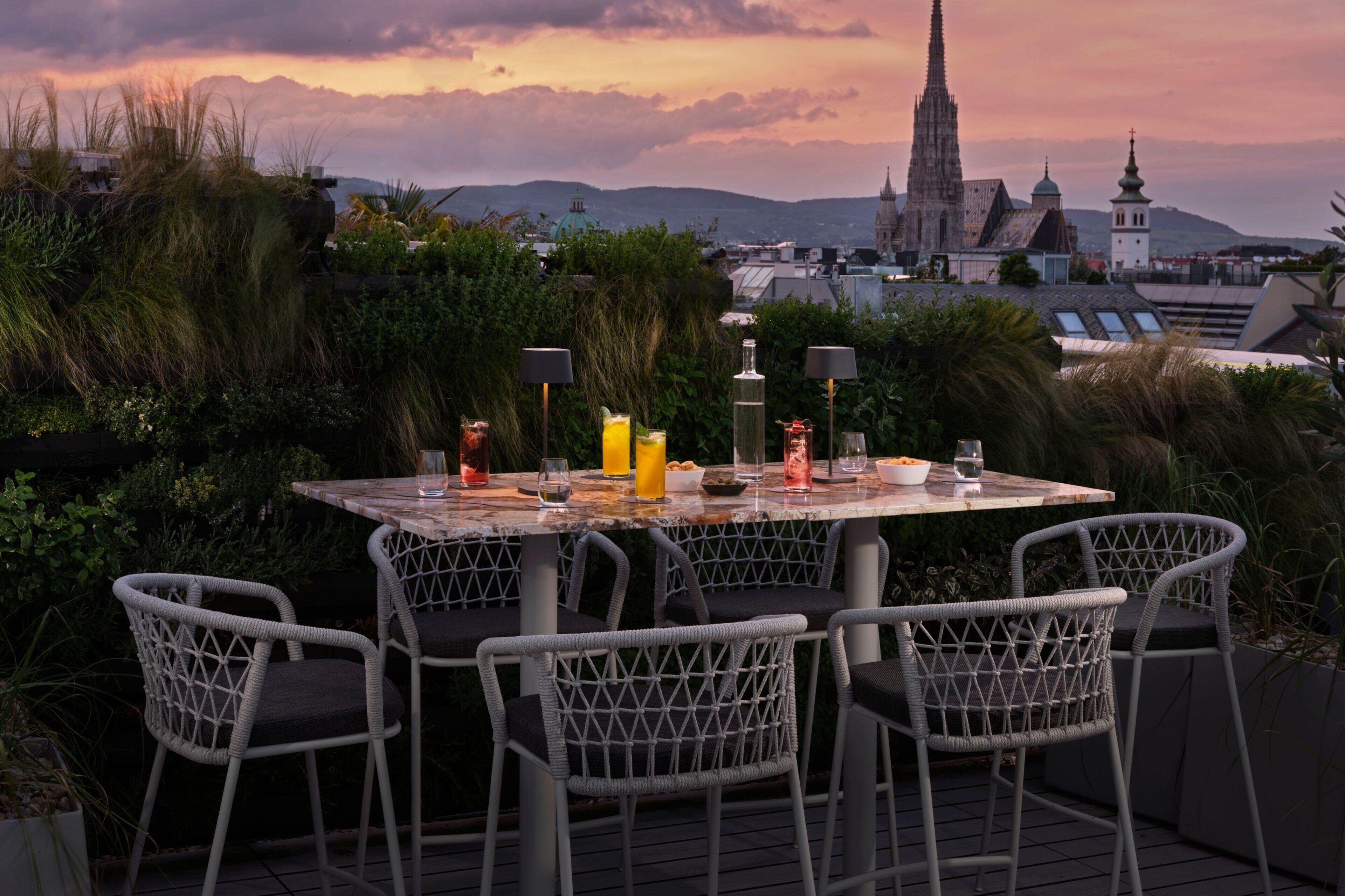 Une table dressée à l’extérieur, avec des chaises, un paysage urbain en arrière-plan et un coucher de soleil.