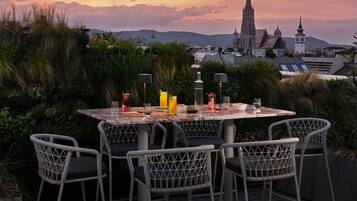 Une table dressée à l’extérieur, avec des chaises, un paysage urbain en arrière-plan et un coucher de soleil.