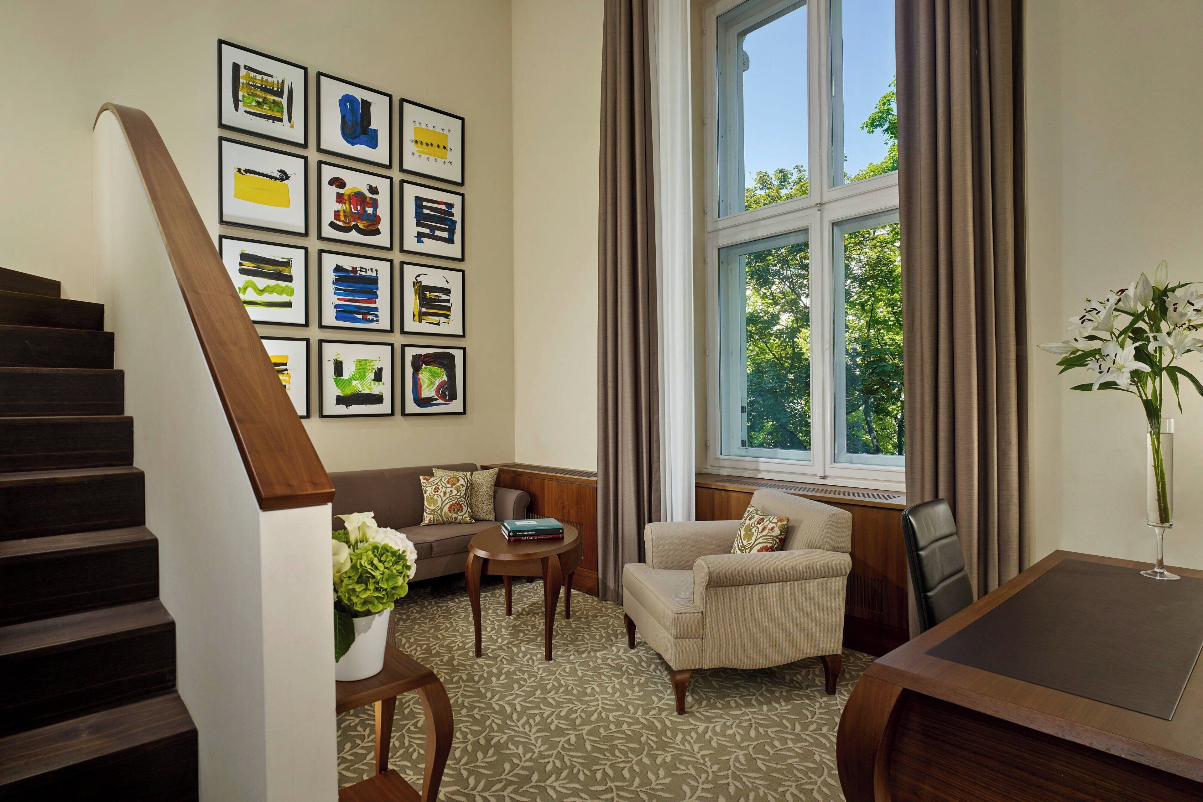 A room with a staircase, a sofa, a chair, a small table, and a window with curtains.