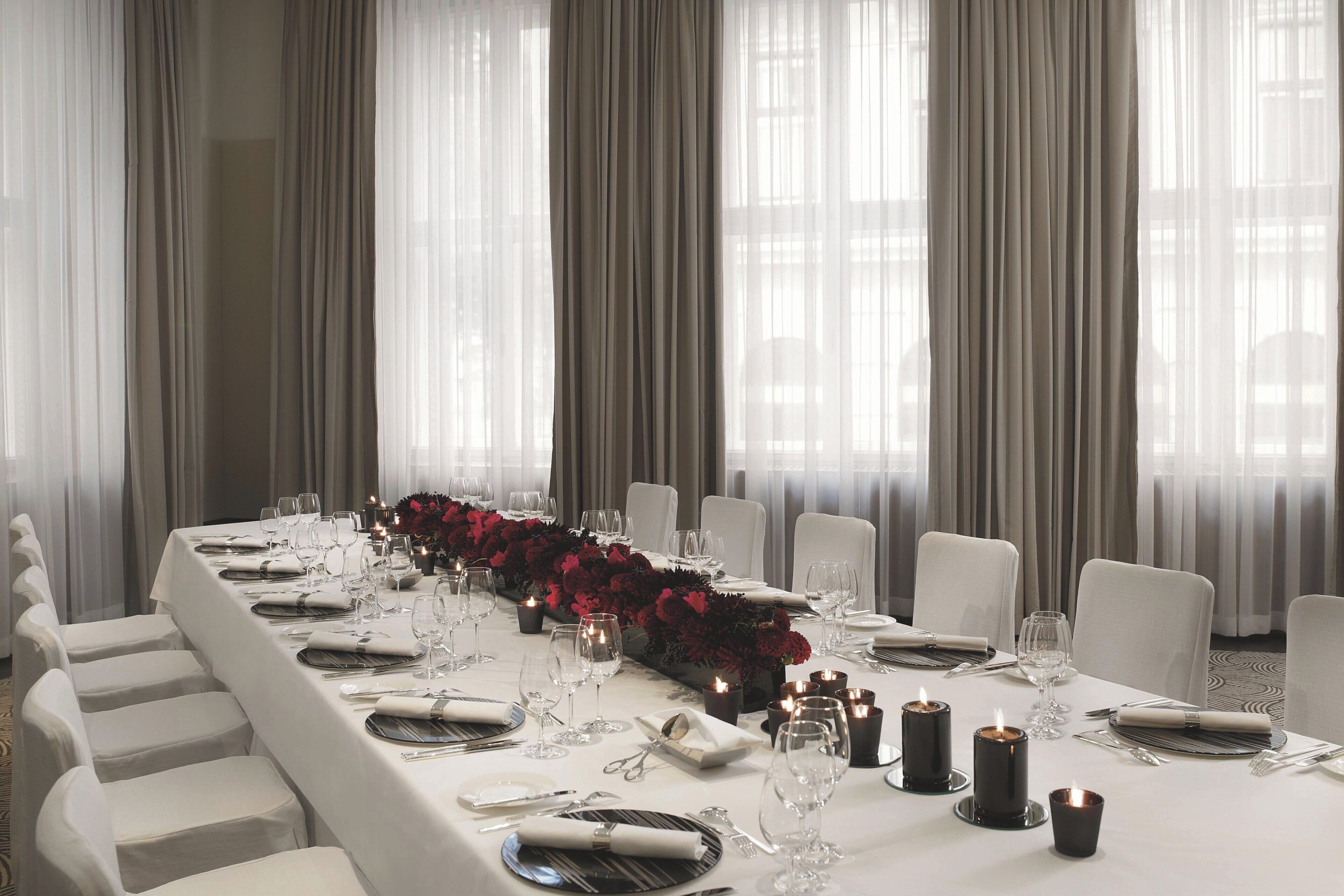 Uma longa mesa de jantar posta para um evento formal, com velas e flores vermelhas.