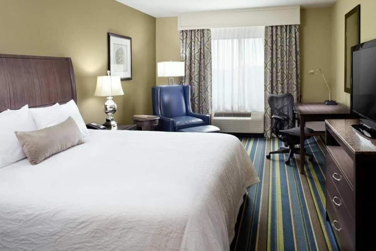 A hotel room with a bed, a desk, a chair, a television, and a window with curtains.