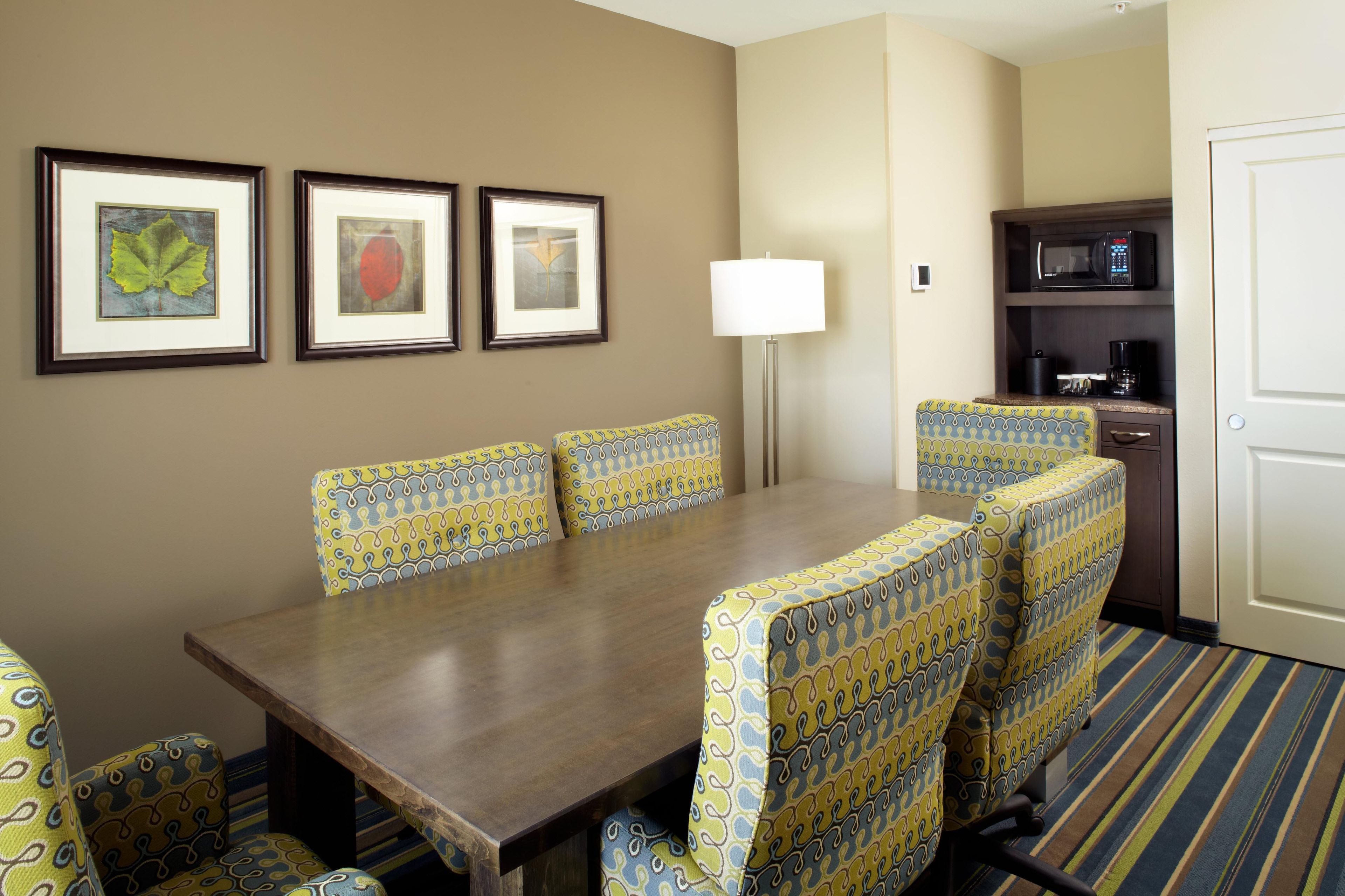 Habitación de hotel con una mesa de comedor, cuatro sillas estampadas, una lámpara de pie, un microondas y una cafetera.