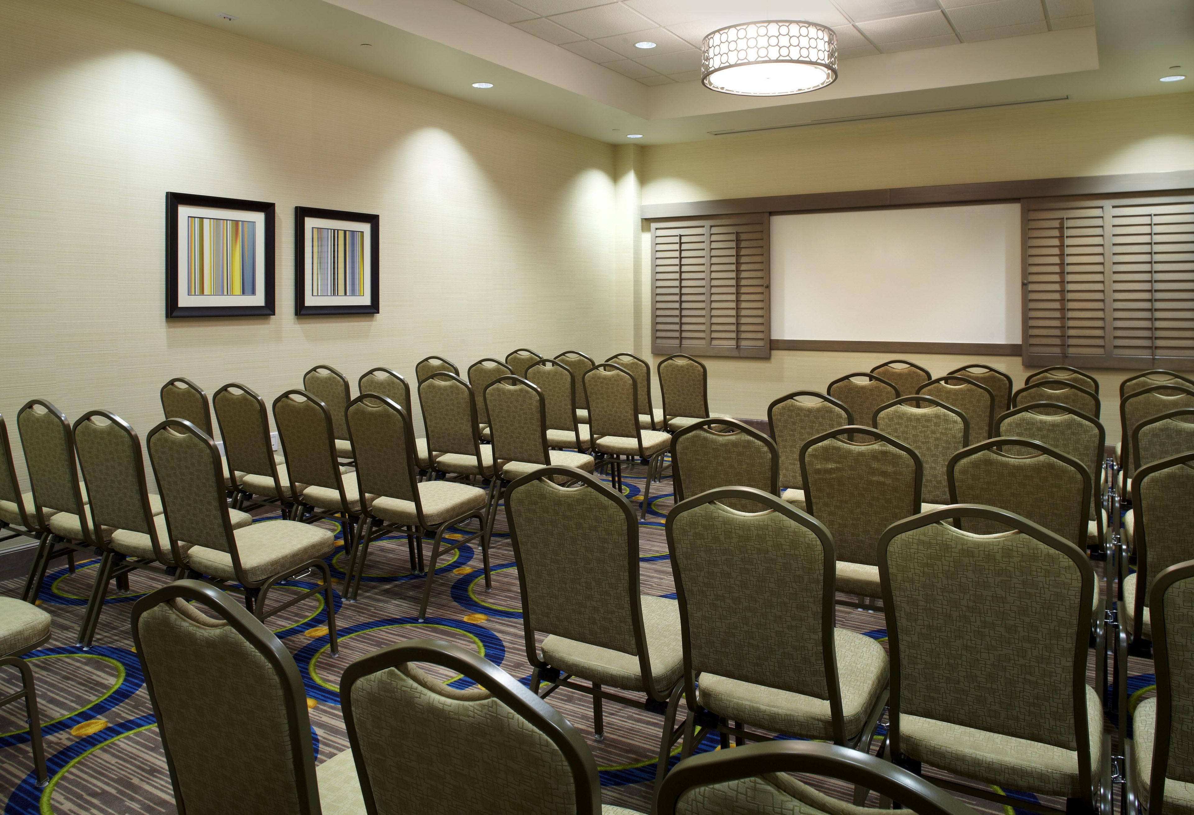 A conference room with rows of chairs, a projector screen, and two framed artworks on the wall.