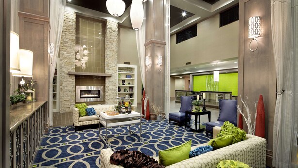 Um lobby espaçoso com carpete azul estampado, área de estar com sofá e poltronas, lareira e luminária moderna.
