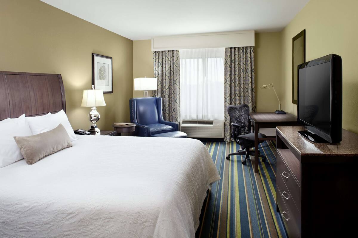 A hotel room with a large bed, a desk with a computer, a TV, and a chair.