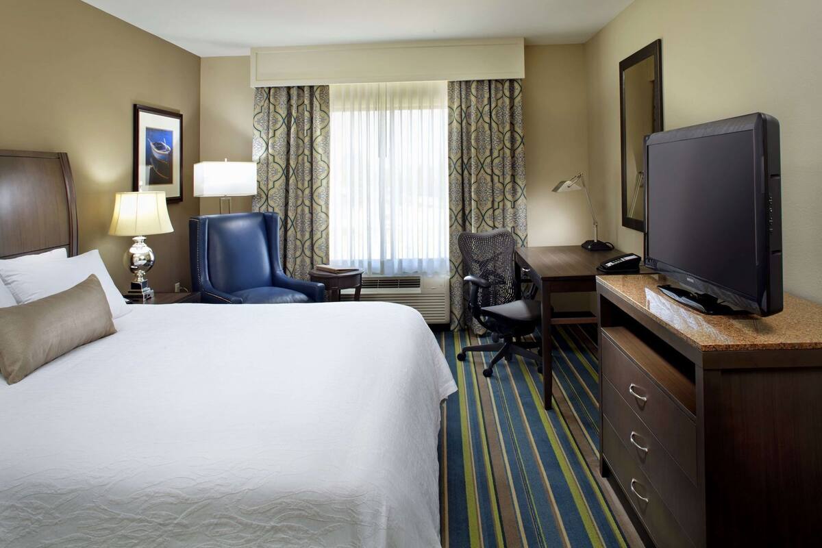 A hotel room with a bed, a desk, a chair, a television, and a window with curtains.