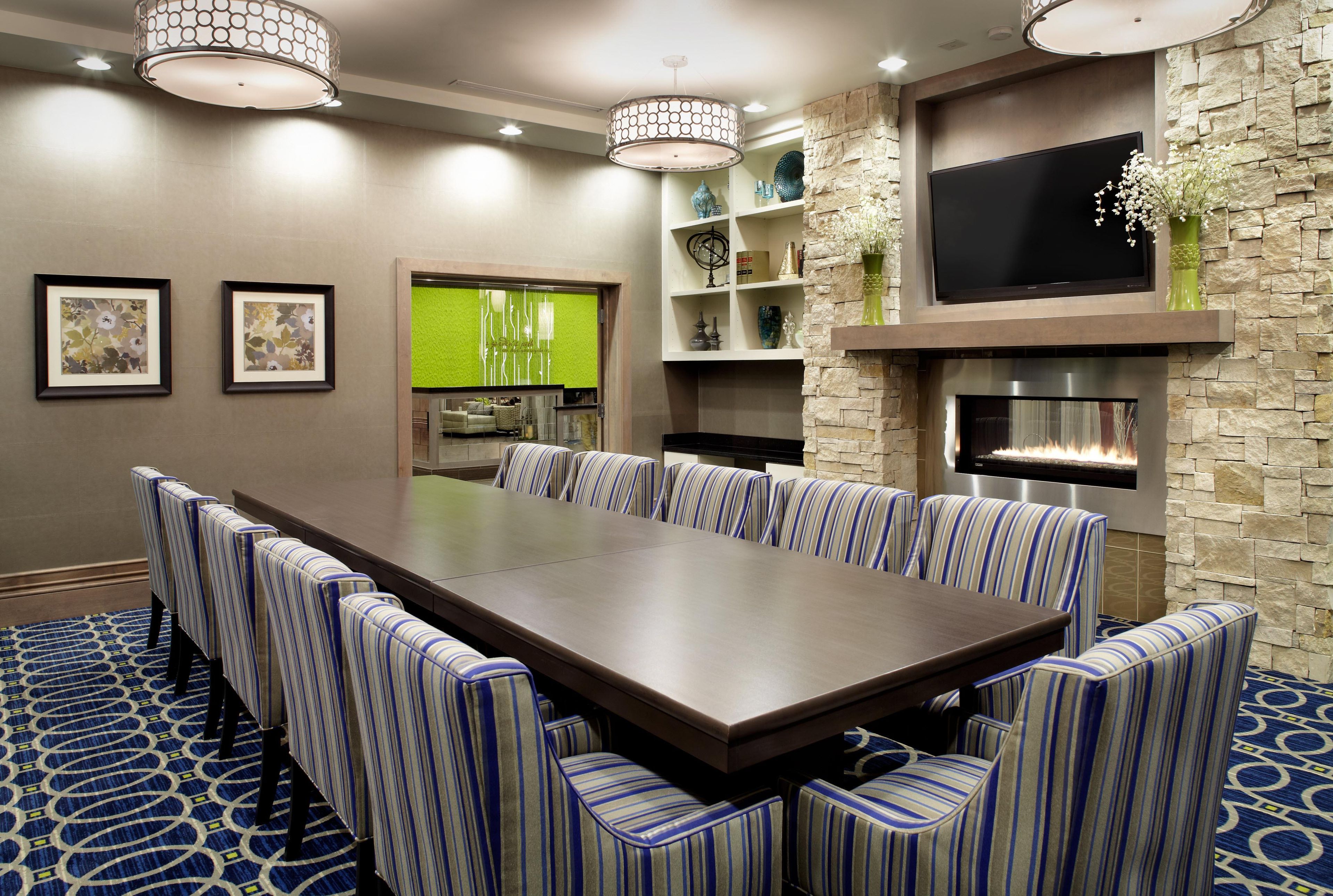 A conference room with a long table, striped chairs, a fireplace, and a television mounted on a stone wall.