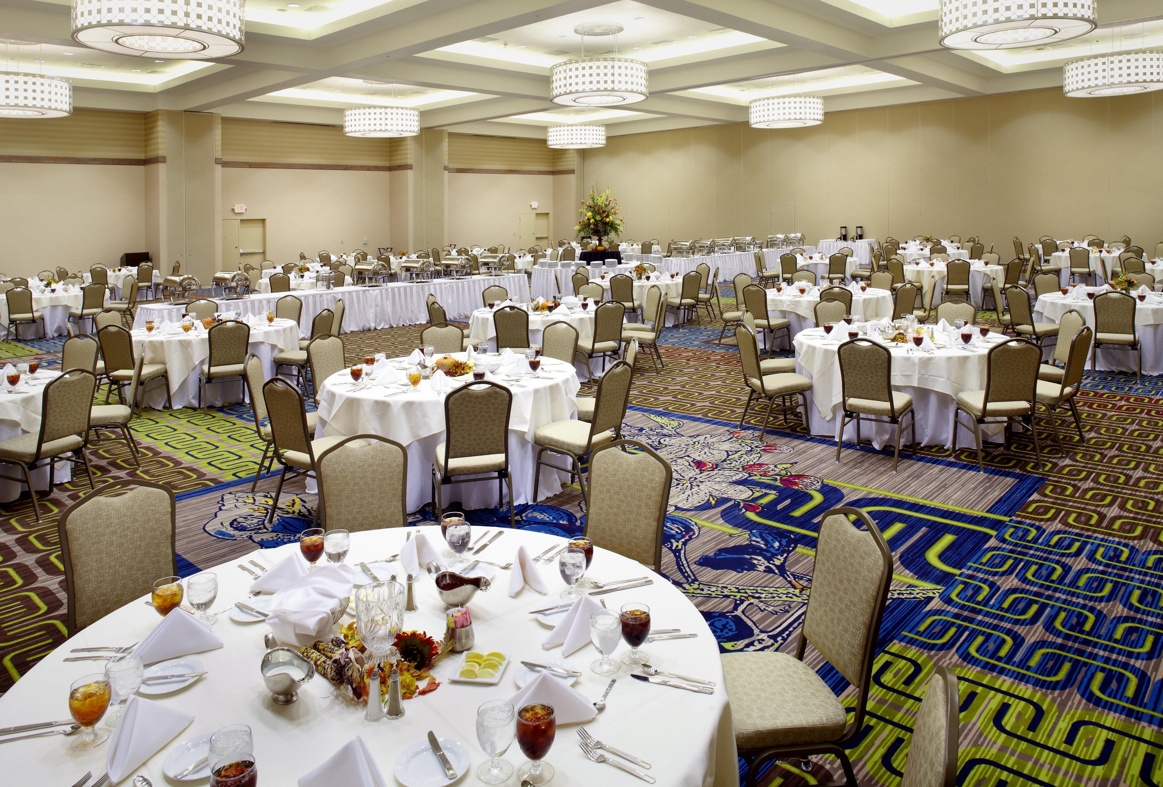 A banquet hall with round tables, chairs, and a patterned carpet.