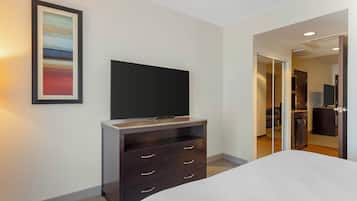 Une chambre d’hôtel avec un lit, une commode en bois foncé dotée de tiroirs, un téléviseur à écran plat fixé au mur et un tableau encadré.