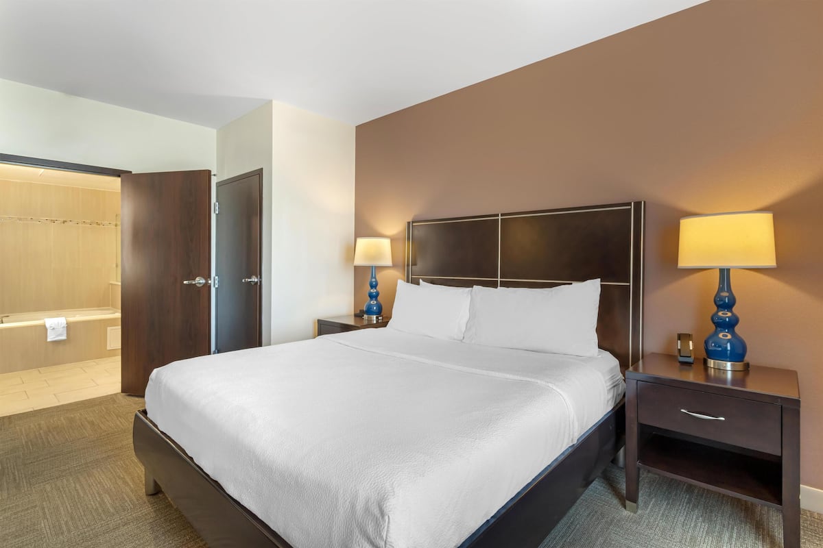 A hotel room with a large bed, two bedside tables with lamps, a wooden wardrobe, and a bathroom with a shower.