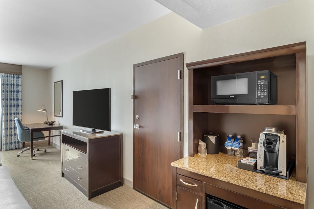 A hotel room with a desk, television, microwave, coffee maker, and storage cabinets.