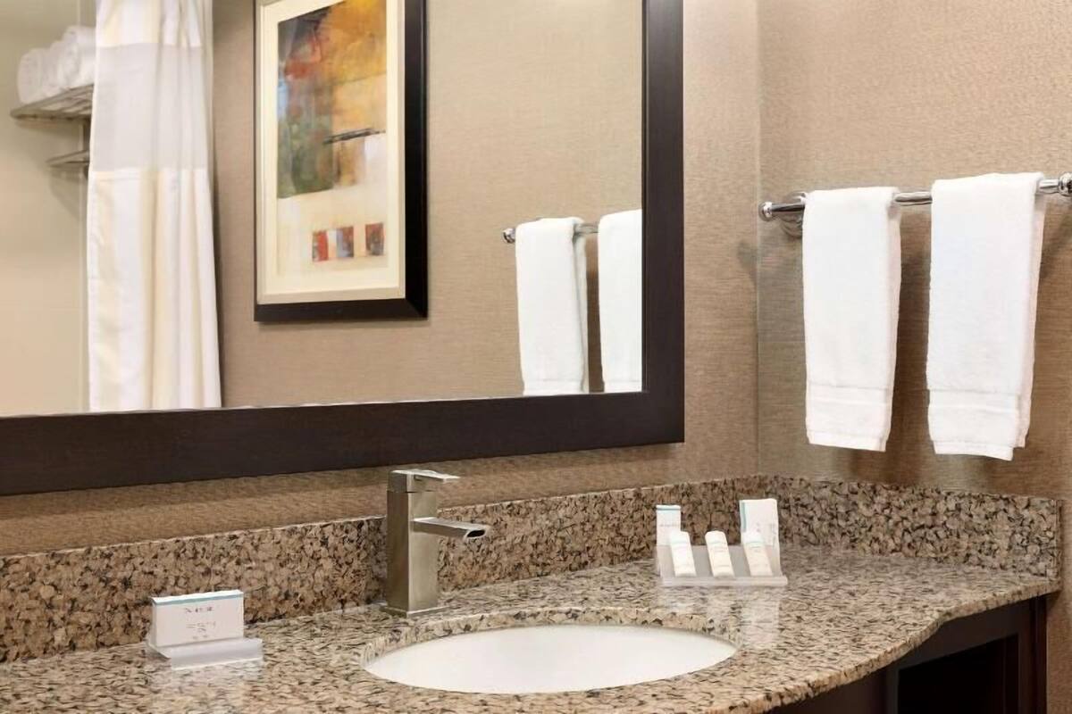 A bathroom with a granite countertop, a sink, a large mirror, and a towel rack with two white towels.