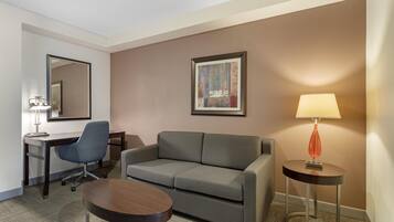 Une chambre d’hôtel avec un canapé, un bureau, une chaise, une lampe et un tableau encadré au mur.