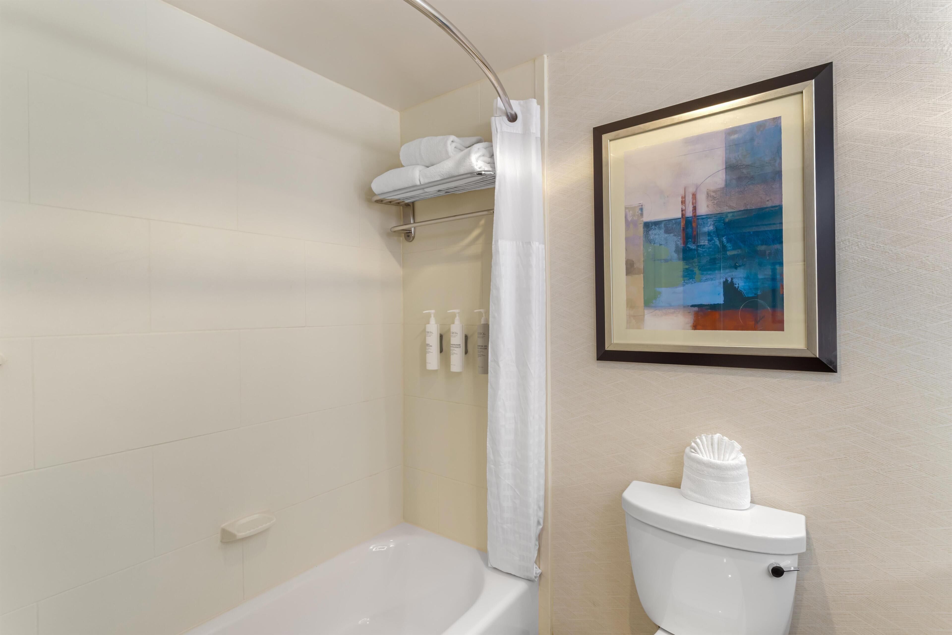 A bathroom with a bathtub, toilet, and a framed abstract painting on the wall.