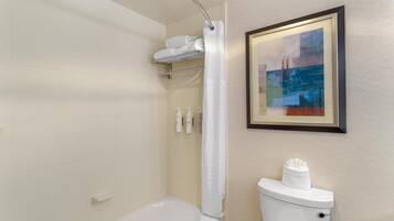 A bathroom with a bathtub, toilet, and a framed abstract painting on the wall.