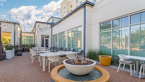 Une terrasse extérieure avec des tables et des chaises, un foyer et un bâtiment doté de grandes fenêtres.