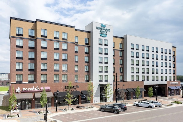 A hotel with a modern design, featuring a mix of brick and white facades, multiple floors, and a parking area with cars.