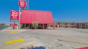 A Red Roof Inn with a red exterior, a visible parking lot with directional arrows, and a clear blue sky. - Red Roof Inn Needles (Needles)